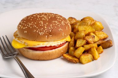 Kızarmış yumurta ve peynirli domatesli susamlı çörek ve patates kızartması.