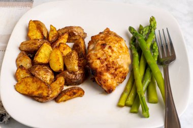 kuşkonmaz ve patates dilimleri ile servis edilen tavuk budu.