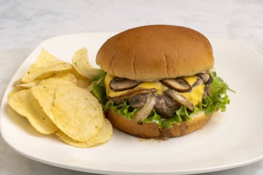 Peynirli burger, soğanlı ve mantarlı. Patates cipsiyle servis edilen bir çörek., 