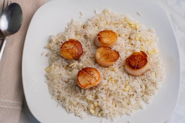 Beyaz pirinçle servis edilen tavada istiridye soğan ve sarımsak var.