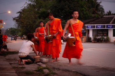 Luang Prabang, Laos - 9 Nisan 2011: Sabah erken saatlerde rahiplerin geçit töreni, 05: 30 sıralarında başladı: Safran cüppeli keşişler ve acemiler yardım kaseleri ('bat') ile sokaklara çıktılar. Onları Lao 'lular bekliyor. Zaman ayırdılar bile. 