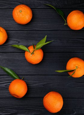 Siyah arka planda yeşil yapraklı taze narenciye meyvelerinin üst görüntüsü.