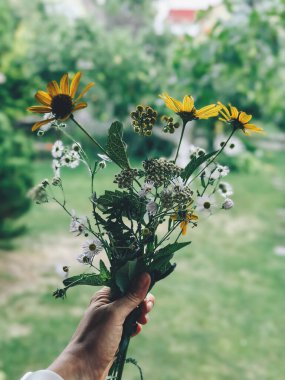 Bir buket taze koparılmış kır çiçeğini tutan yeşil arka planlı bir kadın.