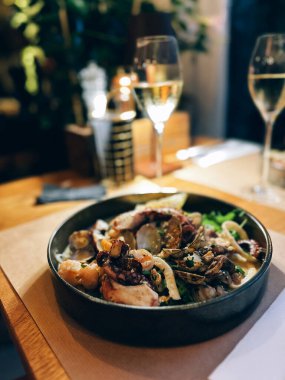 Lezzetli deniz ürünleri bir restoran masasında iki bardak beyaz şarapla servis edilir.