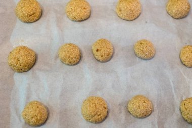 Pişirme tepsisine yerleştirilmiş kurabiyeler, fırına hazır. Hamur topları parşömen kağıdına eşit aralıklarla konur. Pişmemiş yiyecekler altın kahverengidir. Yulaf ezmesi ya da benzer malzemeler olabilir. Hazırlık aşaması yakalandı
