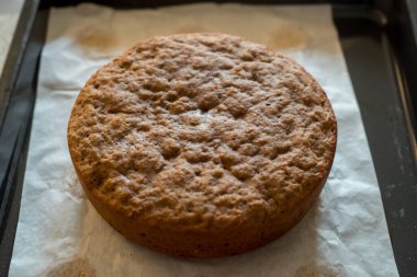 Parşömen kâğıdının üzerine yeni pişmiş yuvarlak pasta. Fırın tepsisine konmuş. Kalıplı bir yüzeyi olan altın-kahverengi kabuk, yumuşak bir iç yüzeyi gösteriyor. Dekorasyon ve servis için mükemmel bir zemin.