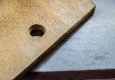 Mutfak masasında tahta kesme tahtası. Pürüzsüz açık kahverengi yüzey, görünür tahıl desenli. Yuvarlak kenar ve köşe görüş alanında. Günlük mutfak kullanımı için işlevsel araç.