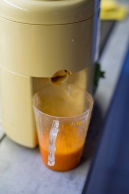 Meyve sıkacağının alt kısmı kabak suyuyla dolu. Şeffaf konteynır ve canlı turuncu sıvı odak sağlar. Arka plan sessiz mutfak elementleriyle bulanıklaştı.