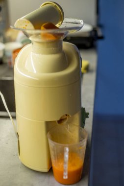 Meyve sıkacağı mutfak tezgahında paraşütün içinde balkabağı ile duruyor. Sıvı aşağıdaki ölçü kabına akıyor. Cihazda krem vücut var. Taze içecek hazırlama süreci. Arkaplan bulanık