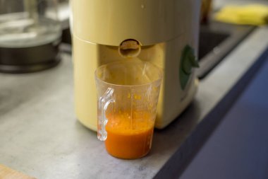 Meyve sıkacağının alt kısmı kabak suyuyla dolu. Şeffaf konteynır ve canlı turuncu sıvı odak sağlar. Arka plan sessiz mutfak elementleriyle bulanıklaştı.