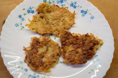 Beyaz tabakta kızarmış patatesli krep, çiçek desenli, mavi çiçekler. Üç altın kahverengi parça. Ahşap yüzey arka planı. Basit sunum, köy mutfağı..