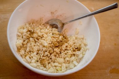 Doğranmış soğan, un ve baharatlarla birlikte derin beyaz kasede yemek kaşığıyla. Parçalar eşit kaplanmış. Ahşap yüzey çanak tutuyor. Basit hazırlık tamamlandı. Lezzetli yemek kızarmaya hazır..