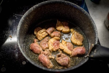 Tavada kızarmış ördek eti. Parçalar cızırdıyor. Yağ köpürüyor. Siyah yüzey görünüyor. Meyve suları parlıyor. Kenarları gevrek. Yemek pişirme devam ediyor. Zengin aromalı mutfak. Ilık ışıklandırma. Ev hazırlığı.
