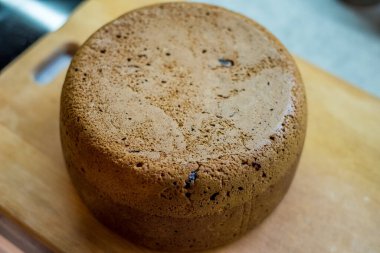 Tahtaya yerleştirilmiş büyük vişneli pasta, altın hamuru pişmiş dokuyu, küçük çatlakları, dağınık noktaları gösteriyor. Taze sünger nazikçe soğur, dilimlenmeye hazır, sıcak ev yapımı toplanma sırasında paylaşılır..