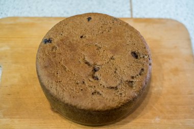 Tahtaya yerleştirilmiş büyük vişneli pasta, altın hamuru pişmiş dokuyu, küçük çatlakları, dağınık noktaları gösteriyor. Taze sünger nazikçe soğur, dilimlenmeye hazır, sıcak ev yapımı toplanma sırasında paylaşılır..