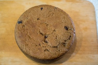 Tahtaya yerleştirilmiş büyük vişneli pasta, altın hamuru pişmiş dokuyu, küçük çatlakları, dağınık noktaları gösteriyor. Taze sünger nazikçe soğur, dilimlenmeye hazır, sıcak ev yapımı toplanma sırasında paylaşılır..