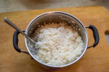 Pişmiş pirinç tencerenin içinde nazikçe yerleştirilmiş kaşıkla dinleniyor. Buhar yavaşça akıyor. Basit mutfak atmosferi sıcaklık, tat, doku, durgunluk, denge, ışık, bakım, konfor öneriyor.