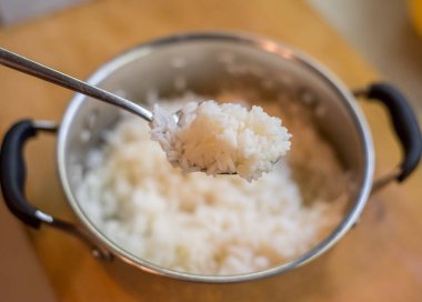 Pişmiş pirinç tencerenin içinde nazikçe yerleştirilmiş kaşıkla dinleniyor. Basit mutfak atmosferi sıcaklık, tat, doku, durgunluk, denge, ışık, bakım, konfor öneriyor.