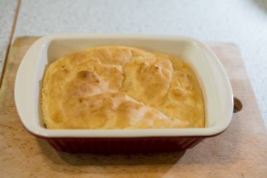 Taze pişmiş somun, güverteye yerleştirilmiş seramik tabağın içinde duruyor. Ekmek yüzeyi altın gibi görünüyor ve biraz düzensiz. Kenarları yavaşça yükseliyor. Arka plan yumuşakça harmanlanır, rahat mutfak havasını arttırır..