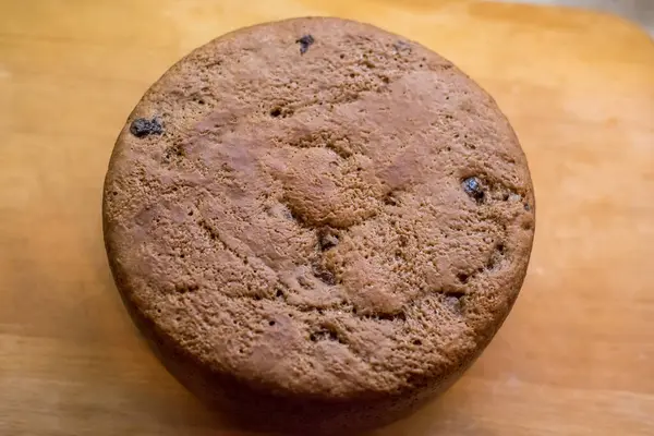 Tahtaya yerleştirilmiş büyük vişneli pasta, altın hamuru pişmiş dokuyu, küçük çatlakları, dağınık noktaları gösteriyor. Taze sünger nazikçe soğur, dilimlenmeye hazır, sıcak ev yapımı toplanma sırasında paylaşılır..