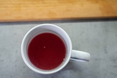 Kupa, iç boşluğu dolduran kırmızı komposto içeriyor. Konteynır ahşap masa yüzeyinin üzerinde duruyor. Mutfak alanı yemek hazırlama anlamına geliyor. Sapı sağdan dışa doğru uzanıyor. Sıvı parlak parlaklığı gösterir.