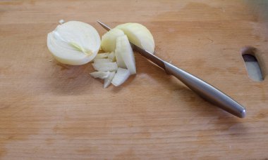 Kesme tahtasında bıçak ve soğan var. Bıçak sebzeye yakın bir yerde. Dilimler halinde görünen katmanlar. Düzenleme yemek hazırlamayı öneriyor. Malzemelerin karşıtlığı ayrımı vurgular.