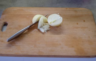 Kesme tahtasında bıçak ve soğan var. Bıçak sebzeye yakın bir yerde. Dilimler halinde görünen katmanlar. Düzenleme yemek hazırlamayı öneriyor. Malzemelerin karşıtlığı ayrımı vurgular.