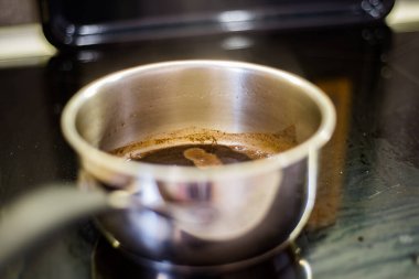 Metal kap, siyah cam yüzeyin üzerinde taze demlenmiş kahve içerir. Buhar koyu sıvı üzerinde sürüklenir. Konteynır tabanının altında yansıtıcı ışıltılar var. Sabah içkisi