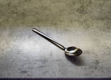 Çay kaşığı gri mutfak tezgahında duruyor. Çapraz yerleştirilmiş metal aletler. Tezgah sade bir görünüm sergiler. Nesne temiz bir tasarım gösteriyor. Yerleştirme basit kalıyor, tam olarak. Edge net, saf işaret verir, geçerlidir.