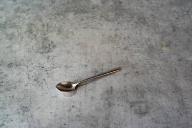 Çay kaşığı gri mutfak tezgahında duruyor. Çapraz yerleştirilmiş metal aletler. Tezgah sade bir görünüm sergiler. Nesne temiz bir tasarım gösteriyor. Yerleştirme basit kalıyor, tam olarak. Edge net, saf işaret verir, geçerlidir.