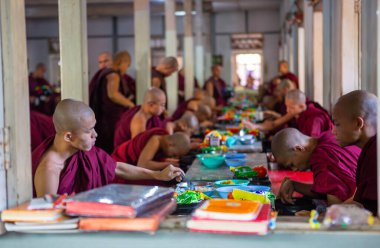 Mandalay, Myanmar, 15 Kasım 2016: Etrafı çok sayıda turistle çevrili genç Budist keşişler, her sabah erkenden kahvaltı için dua üstüne yemek için gemilerle sıraya girerler.