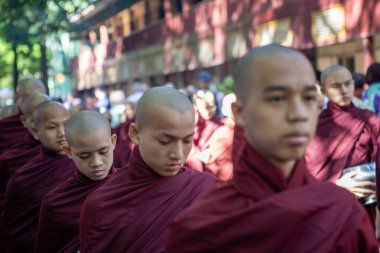 Mandalay, Myanmar, 15 Kasım 2016: Etrafı çok sayıda turistle çevrili genç Budist keşişler, her sabah erkenden kahvaltı için dua üstüne yemek için gemilerle sıraya girerler.