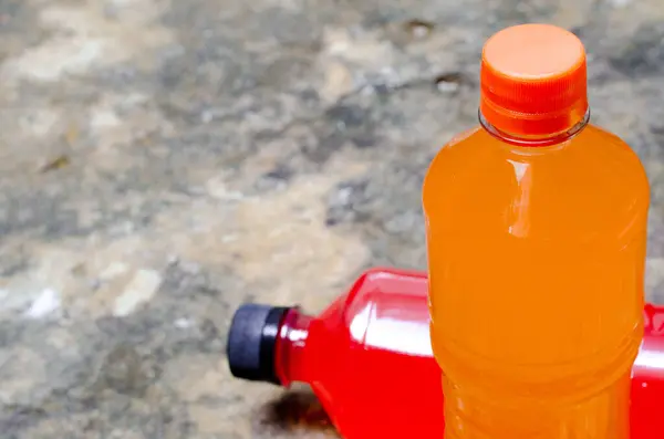 Hydrating, isotonic, sports drink, replenishes electrolytes. Red and orange drink in transparent bottle on rustic stone and cement background. Copy space. Drink for sportsmen in gyms. Real drink.