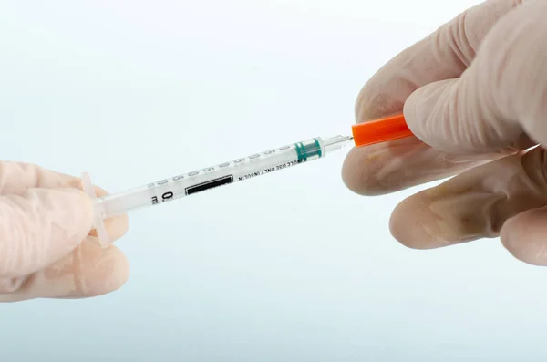 Syringe with needle for insulin isolated on light blue background with orange caps in hands of doctor in white gloves. Medical instruments for diabetes. Closed angle, close-up. Copy space.Real people.
