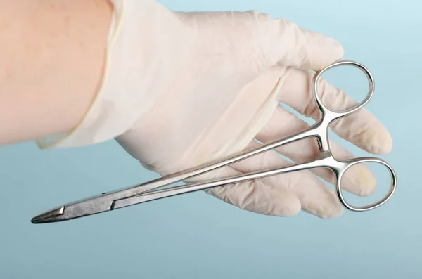 Needle holder for surgical instrumentation table, on white gloves in the hands of a surgeon. Light blue background, closed angle, close up. Real people.