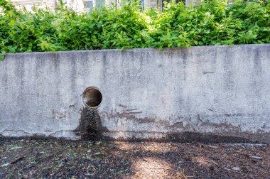 Beton bir bariyerin rengini bozan sızıntılı bir kentsel alanda fırtına suyu boşaltma kanalı. Yüksek kalite fotoğraf