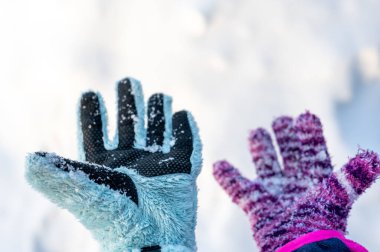 A pair of mismatched gloves on a child held over a white snow background. High quality photo