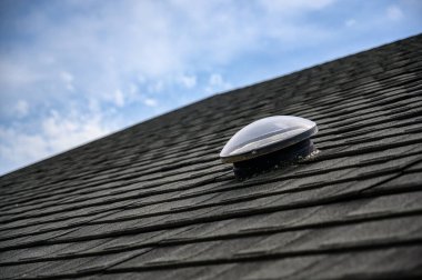 Dome shaped solar tube skylight on asphalt shingle roof . High quality photo