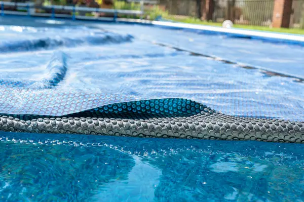Retractable floating pool cover to keep out leaves and keep in heat being pulled back from water. . High quality photo
