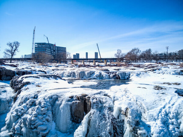 Sioux Falls Park waterfall with ice and snow. Cascading snowmelt water pouring over the top into a pool of standing water. High quality photo