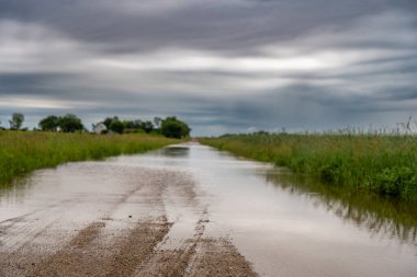 Selective focus on the gravel leading into floodwater covering the road in a rural area. High quality photo clipart