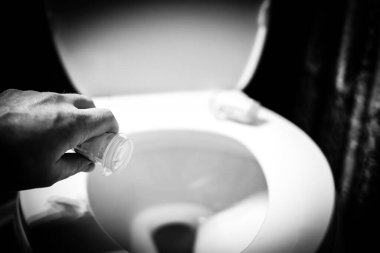 Dumping medication pills from a plastic bottle into an open toilet. High quality photo clipart