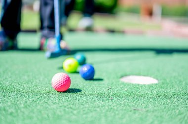 A player stands near colorful golf balls on a mini golf course. The vibrant balls rest on the green turf, ready for the next putt under bright sunlight.