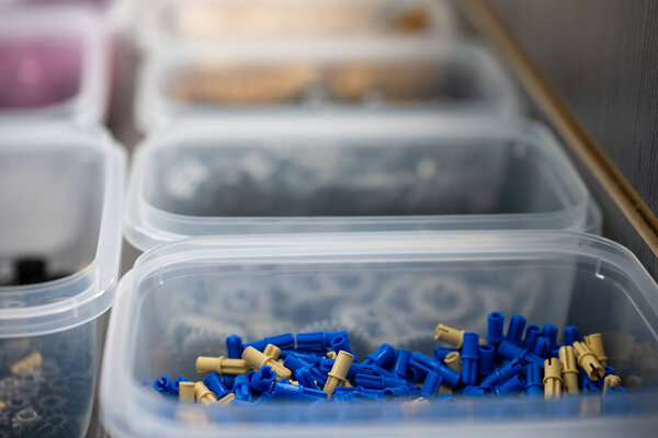 Различные голубые пластиковые разъемы аккуратно расположены в прозрачных контейнерах на рабочем столе. Организация намекает на активное и детализированное рабочее пространство.