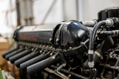 A detailed close-up of a classic car engine is displayed in a workshop, showcasing its intricate design and craftsmanship in natural light during the afternoon hours.