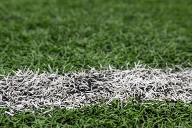 Sahada beyaz bir çizgi işareti gösteren yapay çimlerin yakın görüntüsü. Sahne, çimenliğin canlı yeşilini yakalıyor, oyuna hazır..