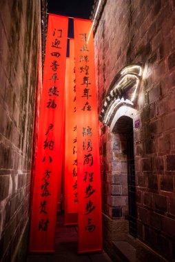 Red vertical banners with new year best wishes written with Chinese script hanging in a narrow street at night in Jinli ancient street, Chengdu, Sichuan province, China