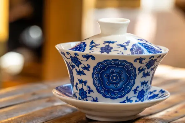 A blue and white porcelain teacup. The teacup is a type of Chinese teacup that has a lid and a saucer. It is typically used for drinking tea from the leaves. The teacup is made of porcelain. The