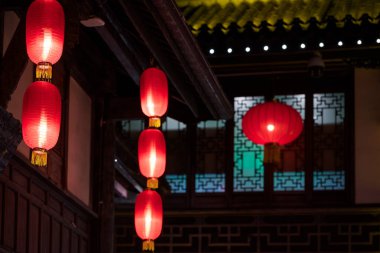 Bir dizi kırmızı fener geleneksel bir Çin avlusunu aydınlatıyor, karmaşık ahşap mimari ve kafes pencereleri sergiliyor..