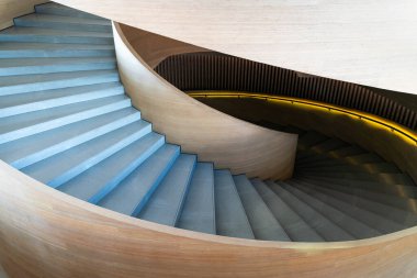 Modern spiral merdiven. Merdiven pürüzsüz, açık renkli ahşapla yapılmış, parlak ve zarif bir görünüm yaratıyor. Basamaklar betondan yapılmış ve ahşap yüzeye zıt bir doku eklenmiş. Tasarım minimalist, temiz.